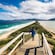 A boardwalk and wooden steps leading down to a verdant, sandy isthmus